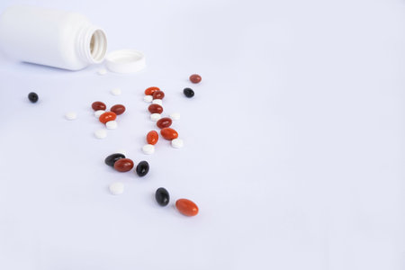 Pills spilling out of pill bottle on white background. Focus on foreground.