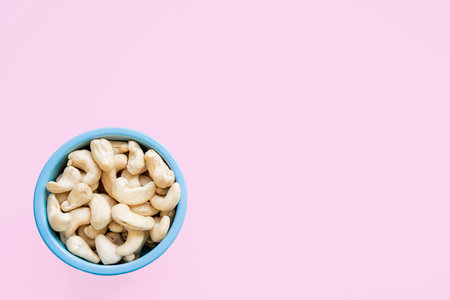 Cashew nuts in blue bowl on pink background. Minimal food concept.の写真素材