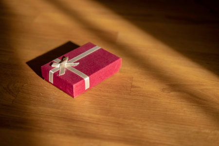 Red gift box on a wooden background with a shadow from the sunの写真素材