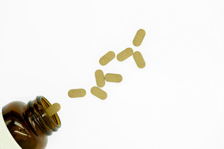 Pills spilling out of a brown bottle isolated on white background.