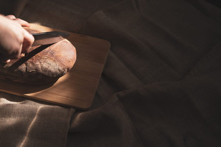 Man cutting a loaf of bread on a wooden board. selective focus.