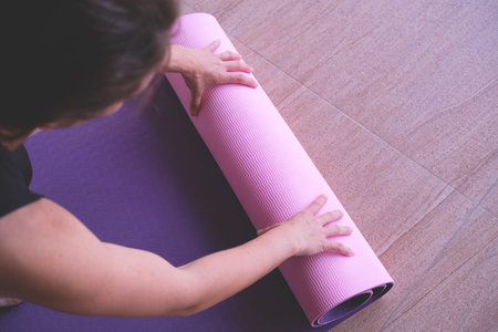 Woman rolling a yoga mat on the floor. View from above.