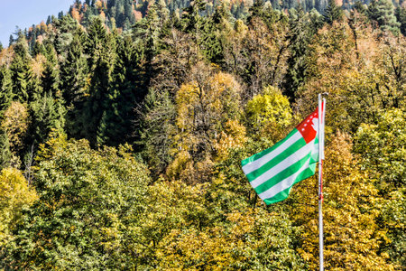 The flag of Abkhazia develops over the autumn mountains.のeditorial素材