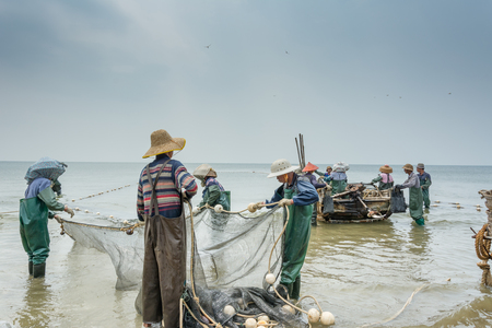 Chinese fishermen taking the fishnet after fishing at the beach against cloudy dayのeditorial素材