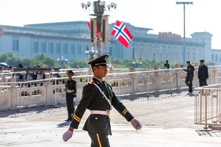 Security guard walking in front of the Tiananmen Gate, at the entrance of the Forbidden City in Beijing, China, 
with the background of Norwegian National flag.のeditorial素材