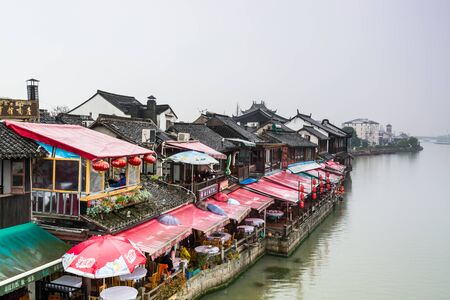Wooden historic buildings at the bank of canal river in Zhujiajiao in a rainy day, an ancient water town in Shanghai, built during Ming and Qing Dynasties of Chinaのeditorial素材
