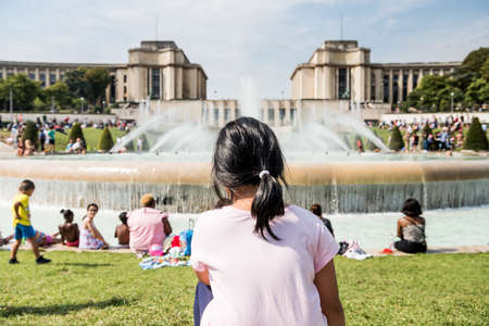 A Chinese kid siting next to the fountain in front of the Palais de Chaillot,  a building at the top of the Chaillot hill in the Trocadero area in the 16th arrondissement of Paris, France.のeditorial素材