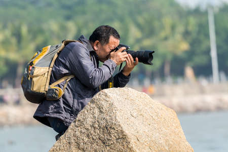 A Chinse photographer holding a Nikon camera to take pictures next to a stone in Shenzhen Bay, Guangdong, Chinaのeditorial素材