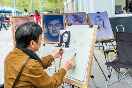 A Shenzhen street artist sketching a picture on the canvas with a pencil iin downtown shenzhen,...