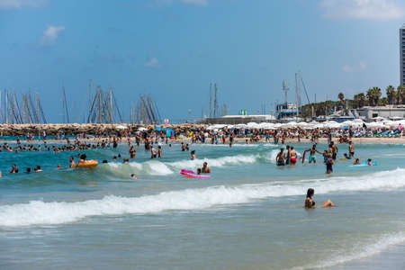 A lot of Tourists and local people enjoy sunbathe, swimming, and sports on a sunny day and the sandy beach of Mediterranean sea coast in Tel Aviv, Israelのeditorial素材