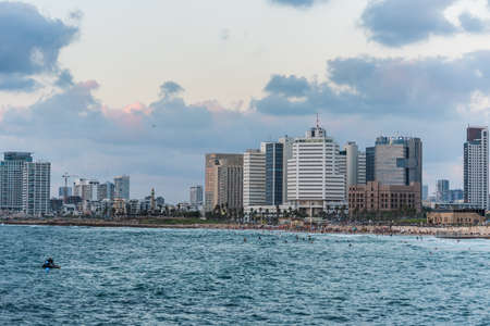 Modern skylines and luxury hotels under twilight at the beach near the old city Jaffa in Tel Aviv, and lots of tourists and locals are swimming in the bay.のeditorial素材