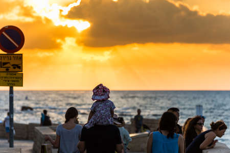 Beautiful sunset and golden twilight, and clouds, Silhouettes of people standing on the coast of Mediterranean sea in Israel and watching the sunset in Tel Aviv, Israel.のeditorial素材