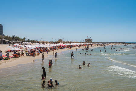 A lot of Tourists and local people enjoy sunbathe, swimming, and sports on a sunny day and the sandy beach of Mediterranean sea coast in Tel Aviv, Israelのeditorial素材
