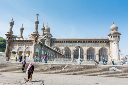 Muslim pilgrims walking into the Mecca Masjid mosque against blue sky and doves flying in sky, a famous monument in Hyderabadのeditorial素材