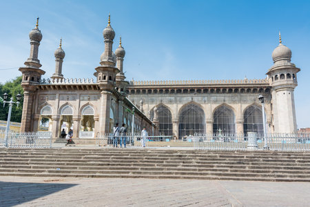 Muslim pilgrims walking into the Mecca Masjid mosque against blue sky and doves flying in sky, a famous monument in Hyderabadのeditorial素材