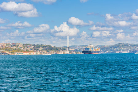 Merchant ship passing through Bosphorus Bridge with background of Bosphorus strait on a sunny day with background cloudy blue sky and blue sea in Istanbul, Turkey. Blue Turkey concept.の写真素材