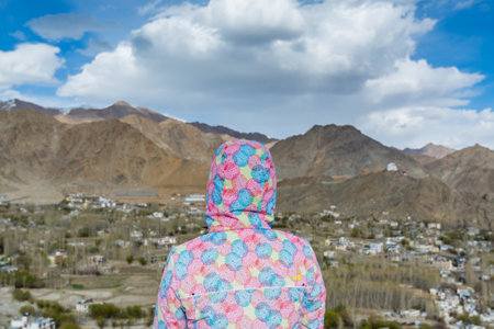 A Chinese female tourist sitting near Shanti Stupa and looking at the Leh Ladahk City of Kashmir with background of Himalaya mountain against blue skyの写真素材