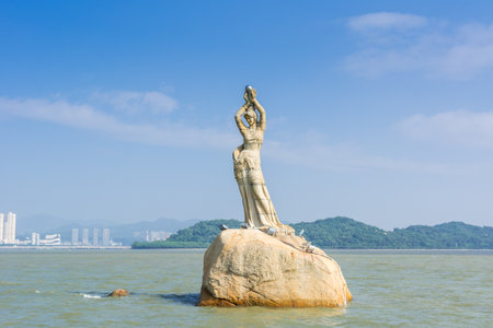 landmark of Zhuhai city of China. Statue of Fish Woman, fisher girl stature with background of sea, island, and tall buildingsの写真素材