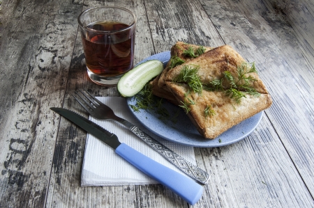 Some sandwiches on the blue plate on the old wooden table. Near knife and fork on the white napkin and glass of tea.の写真素材