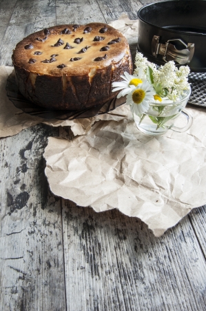 Cheesecake on an old table with a bouquet of daisies and a form for baking. Near wrapping paper. Retro style.From the series "Still Life with cheesecake"の写真素材