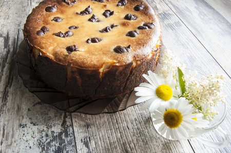 Cheesecake on an old table with a bouquet of daisies and a form for baking. Near wrapping paper....