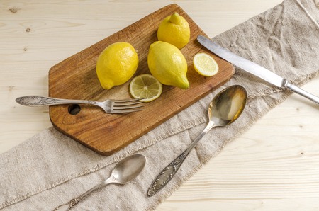 Fruits and slices of lemon on old wooden chopping board, near spoons and forks, linen napkins. Rustic style. Overhead viewの写真素材