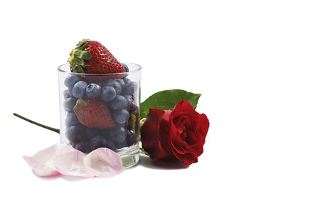 A glass filled with berries and a rose displayed in the white background.の写真素材