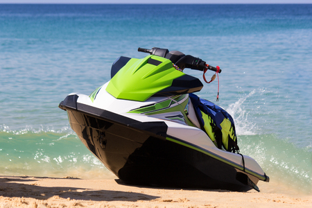 A green-white jet ski is on a beach in waves of blue sea in the sunny weather. Active rest is happy time for all family.の写真素材