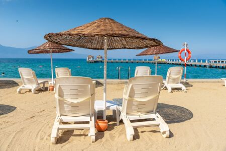 White beach sunbeds and umbrellas put on the beach. Blue sky and mountain in the background. Vacation and holiday on beach concept.の写真素材