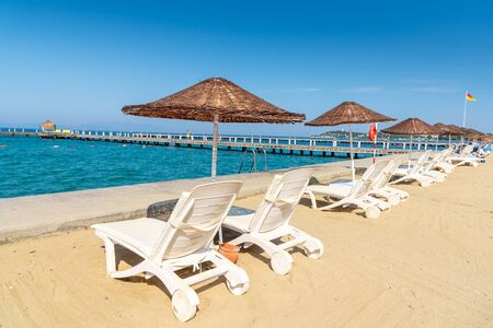 White beach sunbeds and umbrellas put on the beach. Blue sky and mountain in the background. Vacation and holiday on beach concept.の写真素材