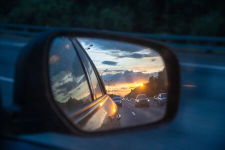 Sunset and beautiful sky is reflected in the mirror of a car. Cars drive along a high road in the evening. Theme of travel by carの写真素材