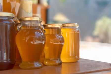 Jars of honey are on the table. Honey is in the lumen. Bokeh background is with sun light. Horizontal close-up. Space for text.の写真素材