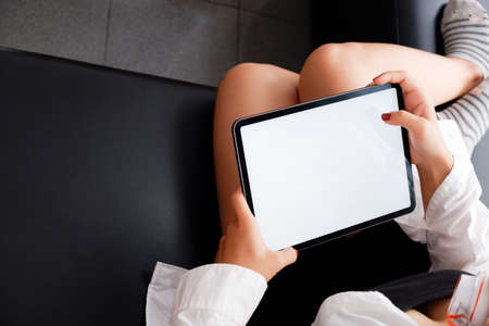 Woman holds tablet in hands. Morning online activities in home. Relax in sofa, watching movies and TV shows on mobile device. Social media addiction. Work at home, freelance. Technology in lifestyleの写真素材