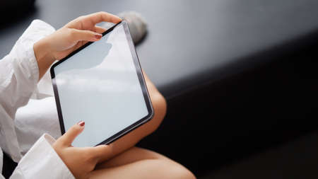 Woman holds tablet in hands. Morning online activities in home. Relax in sofa, watching movies and TV shows on mobile device. Social media addiction. Work at home, freelance. Technology in lifestyleの写真素材