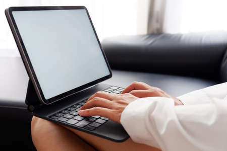 Woman holds tablet in hands. Morning online activities in home. Relax in sofa, watching movies and TV shows on mobile device. Social media addiction. Work at home, freelance. Technology in lifestyleの写真素材