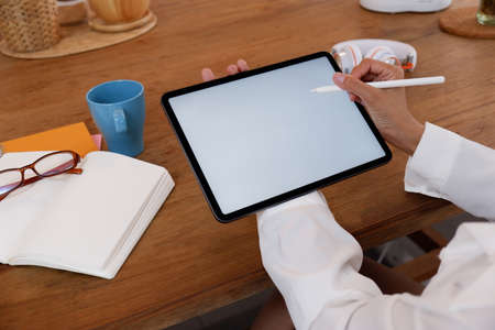 Cropped image of creative woman's hand holding/using a stylus pen to drawing on white blank screen computer tablet that putting on working deskの写真素材