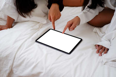 women wake up and wear the comfortable dress on the bed playing tabletの写真素材