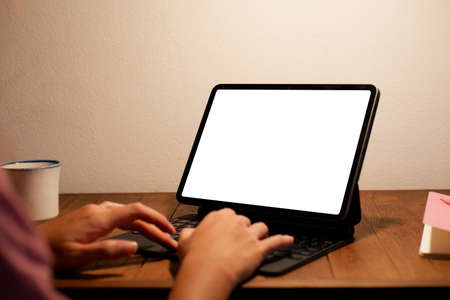 Young woman using black tablet device with white screen. Woman holding tablet, scrolling pages while sitting on the sofa in the living room.の写真素材