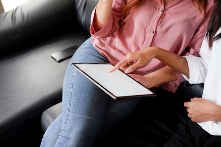 Young woman using black tablet device with white screen. Woman holding tablet, scrolling pages while sitting on the sofa in the living room.の写真素材