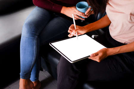 Young woman using black tablet device with white screen. Woman holding tablet, scrolling pages while sitting on the sofa in the living room.の写真素材