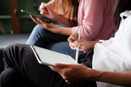 Young woman using black tablet device with white screen. Woman holding tablet, scrolling pages while sitting on the sofa in the living room.の写真素材