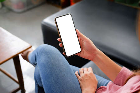 Young woman using black tablet device with white screen. Woman holding tablet, scrolling pages while sitting on the sofa in the living room.の写真素材