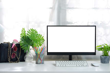 A blank screen computer on a white desk in a woman's workplace with a bag, keyboard, leaves in a bottle,colour pencil.の写真素材