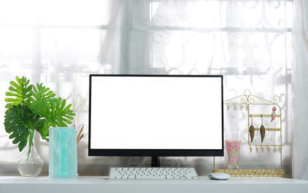 A blank computer screen on a white desk in a woman's workplace with a mask, keyboard, mouse, pencil, leavesの写真素材