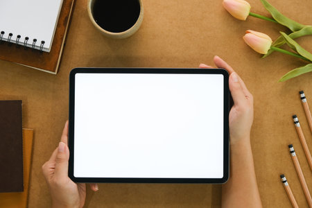 Woman hand holds digital tablet mockup with blank screen, education and application concept template, bright brown background, top view and copy space photo.の写真素材