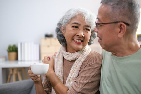 Affectionate senior Asian couple sharing warm embrace on the sofa, celebrating their enduring love and togetherness. Elderly husband and wife happy family.の写真素材