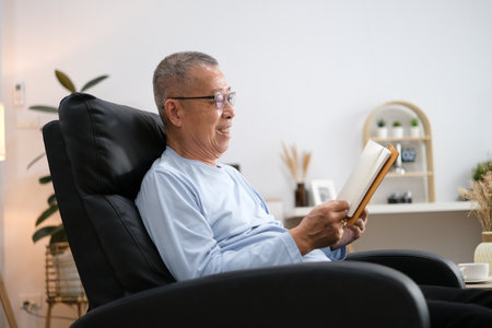 Happy senior Asian man reading book on the chair in living room at home.の写真素材
