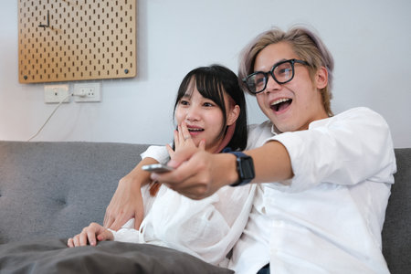 Couple Watches TV together while Sitting on a Couch in the Living Room. Girlfriend and Boyfriend embrace, cuddle, talk, smile and watch Television Streaming Services.の写真素材