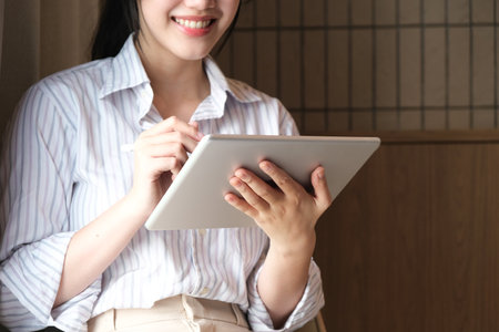 Smiling young Asian business woman leader holding digital tablet standing in office.の写真素材