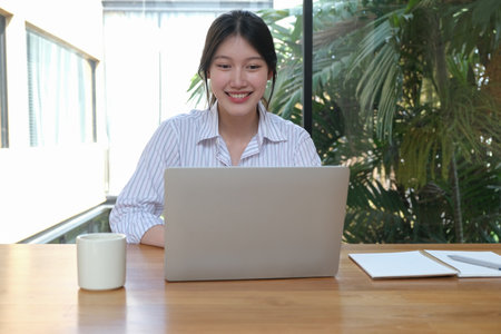 A beautiful girl with a smile on her face communicates with colleagues online, on a laptop.の写真素材
